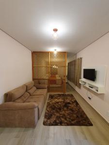 uma sala de estar com um sofá e uma televisão de ecrã plano em Villa Ida Acomodações, 3 suítes aconchegantes e charmosas no centro em Serra Negra