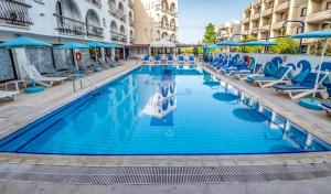 a large swimming pool with blue chairs and umbrellas at Cactus in Larnaka