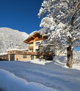 a building covered in snow next to a tree at Ferienwohnungen LODGE-B in Weissenbach am Lech