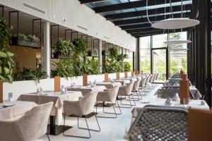 um restaurante com mesas brancas, cadeiras e plantas em Hotel Wiesenhof em Lagundo