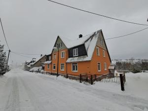 an orange house with a snow covered roof on a snowy street at Ferienwohnung Böhmischerblick in Bärenstein