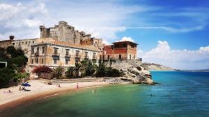 a building on a beach with people in the water at Appartamento Porto Marina S G in Licata