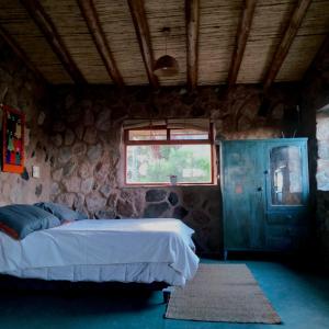 1 dormitorio con cama y pared de piedra en Refugio de Montaña "Casa Chakana " en Ciudad Lujan de Cuyo