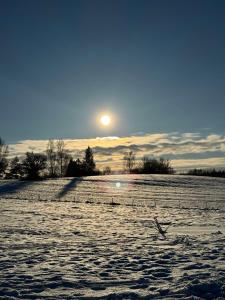 a snow covered field with the sun in the sky at Relax House By The Stone in Nugariai