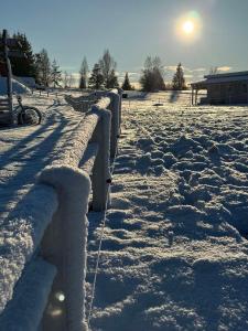 a fence covered in snow with the sun in the background at Relax House By The Stone in Nugariai