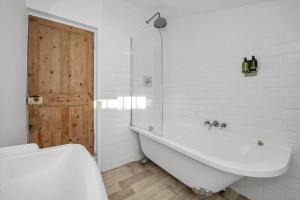 a white bathroom with a tub and a wooden door at 42 Church Row - 2 beds and 2 bathrooms in Bury Saint Edmunds