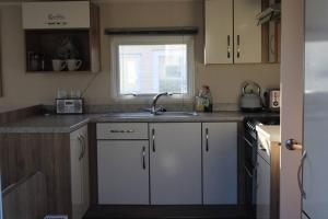 uma cozinha com armários brancos, um lavatório e uma janela em Cosy beachfront getaway in Mersea em West Mersea