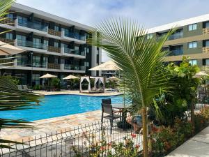 une piscine avec un palmier en face d'un bâtiment dans l'établissement Flat Mana Beach Pono 216 na Praia de Muro alto, à Ipojuca