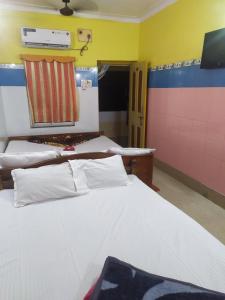 a room with two beds and a tv on the wall at PAYEL LODGE in Digha