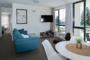 a living room with a blue couch and a table at Ocean View Beach Escape - Top Floor Apartment, Mt Maunganui Base in Mount Maunganui