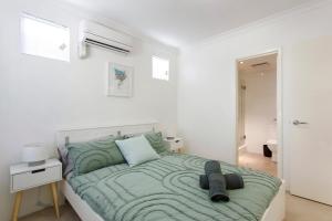 a white bedroom with a bed with a green comforter at Suburban Living - 2 bedroom apartment Victoria Park in Perth
