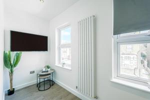 a white living room with a tv and two windows at Stylish Homes W/ Fast Transport Links To London in Bromley