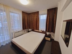 1 dormitorio con 1 cama blanca grande frente a las ventanas en апартаменти Уют Гранд Манастира, en Pamporovo