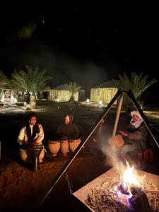 eine Gruppe von Menschen, die um ein Lagerfeuer sitzen in der Unterkunft Nomads Luxury Camp Merzouga in Adrouine