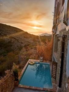 a swimming pool next to a building with a sunset at Casa rural Vall de Gallinera con Chimenea, piscina y jacuzzi DIANIA in Patró