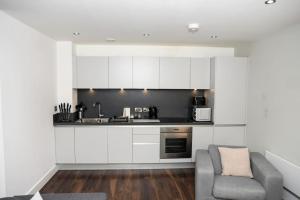 マンチェスターにあるOnPoint - Spacious 2 Bedroom Apt, City Centre!の白いキャビネットとグレーの椅子付きのキッチン