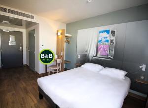 Un dormitorio con una gran cama blanca y una mesa en B&B HOTEL Montélimar Sud en Montélimar