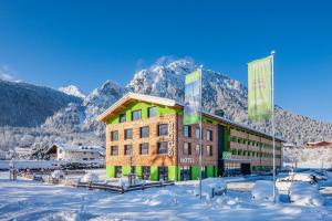 a building in the snow with mountains in the background at Explorer Hotel Berchtesgaden in Schönau am Königssee
