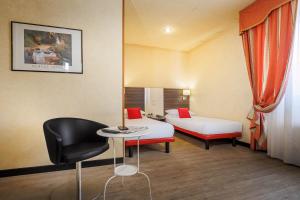 a room with two beds and a chair and a table at JR Hotels Bologna Amadeus in Bologna