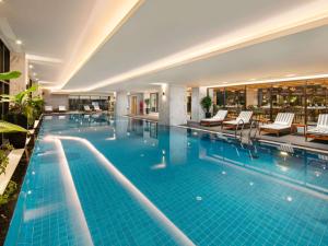 a large swimming pool with chairs and a hotel at Mövenpick Living West Hanoi in Hanoi