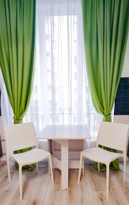 une table et deux chaises avec des rideaux verts dans l'établissement Комфортная студия на Южном вокзале, à Kharkov