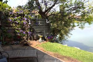 a garden with a bench and flowers next to the water at Cosy home in Pecanwood lake view - Hartbeesport in Hartbeespoort