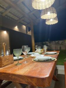 a wooden table with plates and wine glasses on it at Flor de Cacto Beach Home in São Miguel do Gostoso