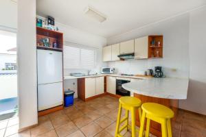 cocina con encimera y 2 taburetes amarillos en On The Beach 19 - Sea View Apartment, en Swakopmund