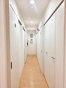 a hallway with white walls and wooden floors and white closets at Shima Stay holoholo in Zamami