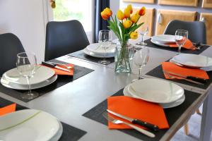 a dining table with plates and glasses and orange napkins at Jolie villa loc-saisonnière - la petite cocagne in Alleins