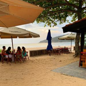 a group of people sitting on the beach under umbrellas at Guaru Surf Hostel in Guarujá