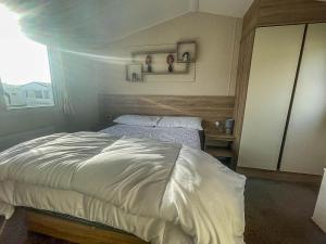 a bedroom with a white bed with a window at Spacious Caravan On The Suffolk Coast With Outside Decking Too Ref 20044bs in Hopton on Sea