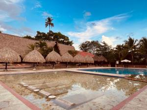 una piscina con sombrillas de paja y un complejo en Hotel Portón del Sol, en Santa Fe de Antioquia