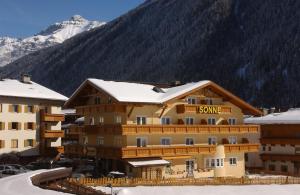 un edificio cubierto de nieve con una montaña en el fondo en Appartements zur Sonne, en Neustift im Stubaital