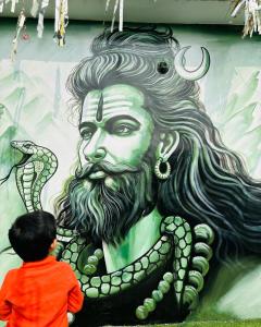 un niño parado frente a una pintura de un hombre con una serpiente en Gully Ghar en Varanasi
