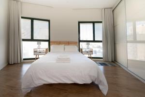een witte slaapkamer met een groot bed en 2 ramen bij Jaffas Yard By IsrApart in Tel Aviv