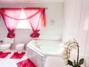 La salle de bains est pourvue d'une baignoire, de toilettes et de rideaux roses. dans l'établissement Tropical Retreat Stay Aruba, à Oranjestad