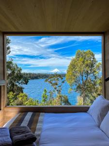 a bedroom with a large window with a view of the water at Exclusiva Cabin en tranquilo campo a orillas del lago con vista a volcanes - hot tub privado in Frutillar