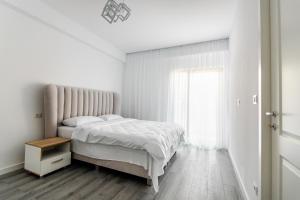 a white bedroom with a bed and a window at Samplus Central Apartment in Craiova