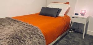a bed with an orange blanket and a side table at Detached Boutique Luxury 3 Bed Villa Free Parking & WI-FI in Kingswood