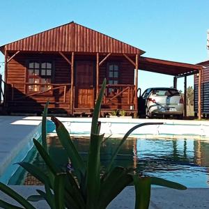 a log cabin with a pool in front of a house at Cabañas Las Escondidas in Chascomús