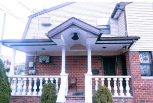 a red brick house with a white front porch at Chic modern bedroom 5 mins from JFK in Locust Manor