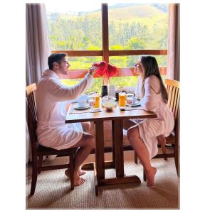 a man and woman sitting at a table with a flower arrangement at Chalés Brisa Da Montanha in Sapucaí-Mirim +6 photos