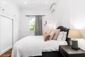 a white bedroom with a bed and a window at La Playa Byron in Byron Bay