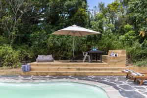 un patio con mesa y sombrilla junto a la piscina en Bitou River Lodge en Plettenberg Bay