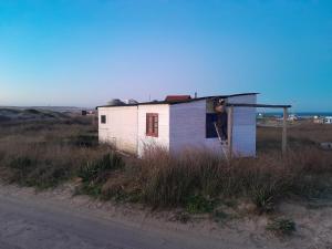 a man standing outside of a small house on the side of a road at Casa de madera en playa de Cabo Polonio con dos ambientes in Cabo Polonio