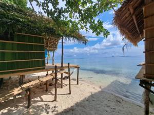 a bench on the beach next to the ocean at Coco Huts Guest House in Waisai
