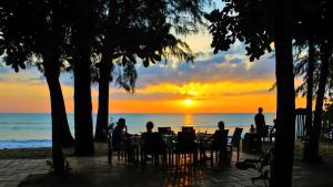 Baan Khaolak Beach Resort في خاو لاك: الناس يجلسون على الطاولات على الشاطئ عند غروب الشمس