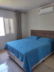 a bedroom with a bed with blue sheets and a window at Casa na praia p aproveitar com a família e amigos in Capão da Canoa