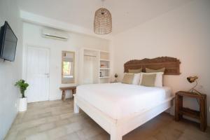 a white bedroom with a large white bed and a television at The Room Padang-Padang in Uluwatu